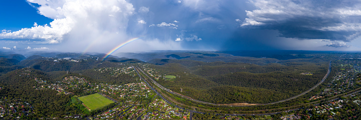 Panoramic view of the M1 Motorway and Pacific Highway Sydney, over Mount Colah with storm clouds and rainbow
