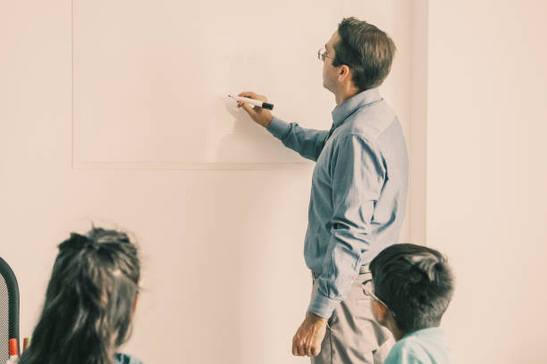 istock Back view of teacher writing on board and explaining lesson 1302401757