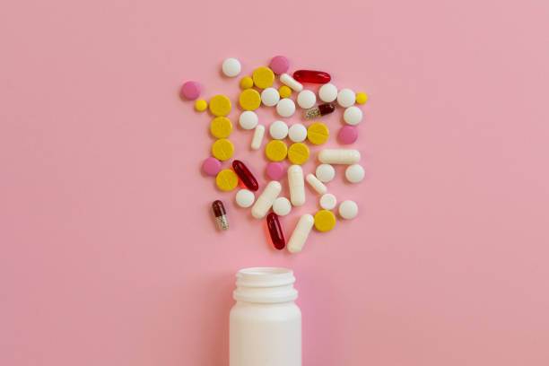 istock Assorted medical pills and capsules scattered from a white plastic bottle on a pink background. 1302402103