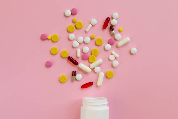 istock Assorted medical pills and capsules scattered from a white plastic bottle on a pink background. 1302402180