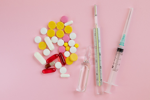 Glass Bottle with medicines. Thermometer, syringe and pill to treat colds on a pink background. Cold remedies. Medical concepts and medicines. Top view.