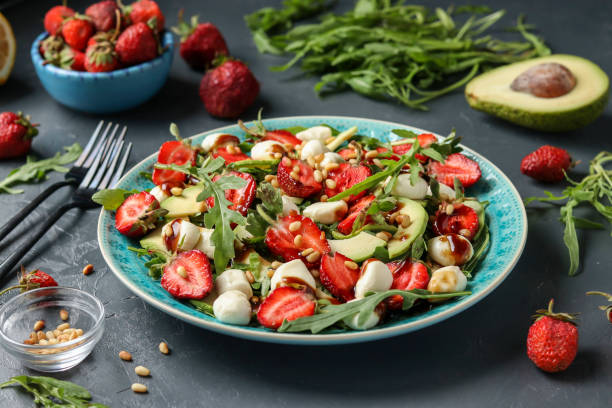 Healthy salad with strawberries, avocado, arugula and mozzarella, dressed with olive oil and balsamic dressing in a blue plate on a dark background, Closeup stock photo