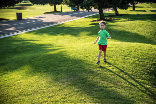 mały chłopiec biegający po trawie na ogromnym polu golfowym - golf child sport humor zdjęcia i obrazy z banku zdjęć