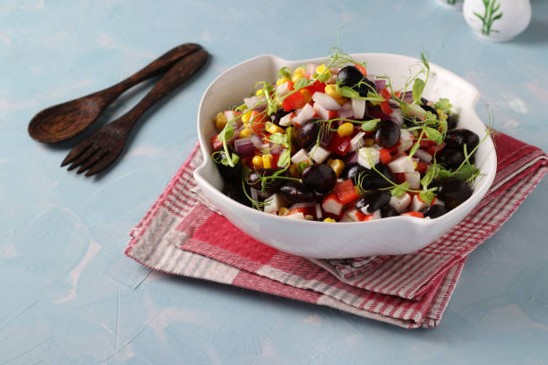 Salad with black beans, corn, crab sticks and peas microgrines in a white bowl on a light blue background, Horizontal format