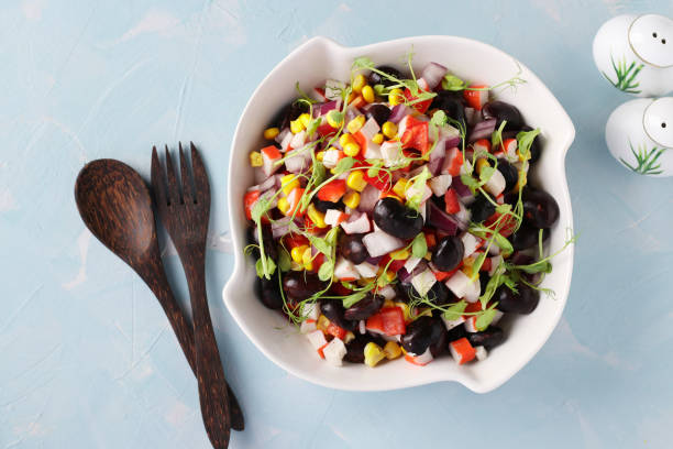 istock Salad with black beans, corn, crab sticks and peas microgrines in a white bowl on a light blue background, View from above 1302404266