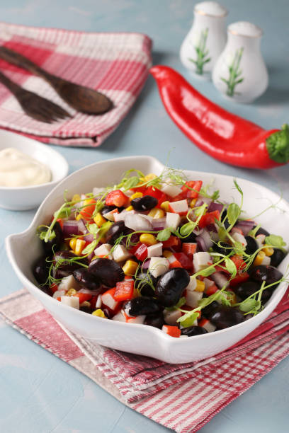 istock Salad with black beans, corn, crab sticks and peas microgrines in a white bowl on a light blue background, Closeup 1302404330