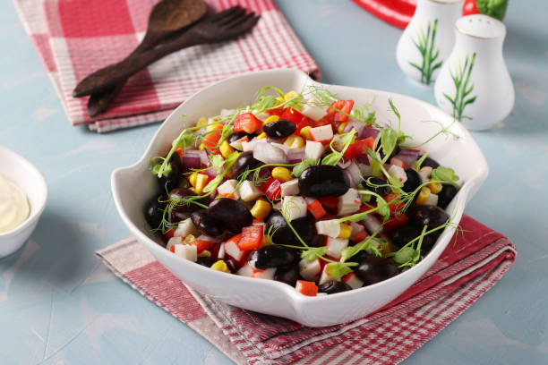 istock Salad with black beans, corn, crab sticks and peas microgrines in a white bowl on a light blue background, Horizontal format 1302404331