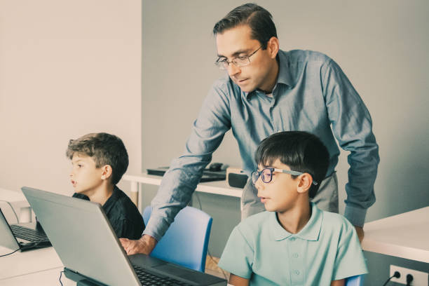 istock Teacher in glasses standing behind pupil and checking task 1302408118