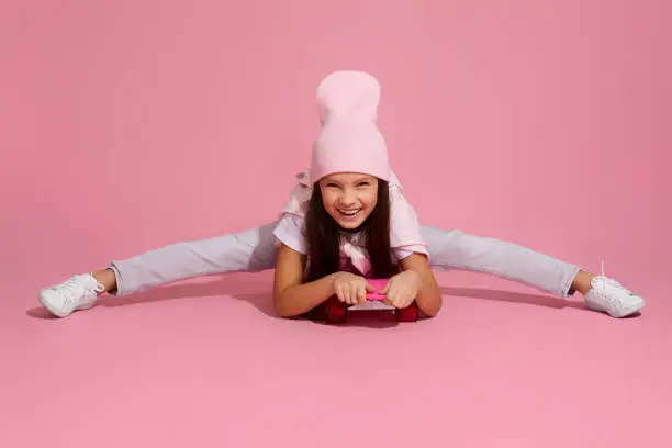 Photo of child girl laughing and sitting on pink skateboard