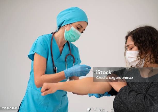 พยาบาลหญิงสวมชุดป้องกันฉีดวัคซีน Covid19 เข้าที่แขนผู้ป่วย ภาพสต็อก - ดาวน์โหลดรูปภาพตอนนี้