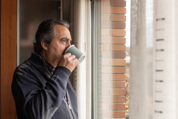 homme avec une tasse regardant par la fenêtre - homme mug regarder dehors photos et images de collection