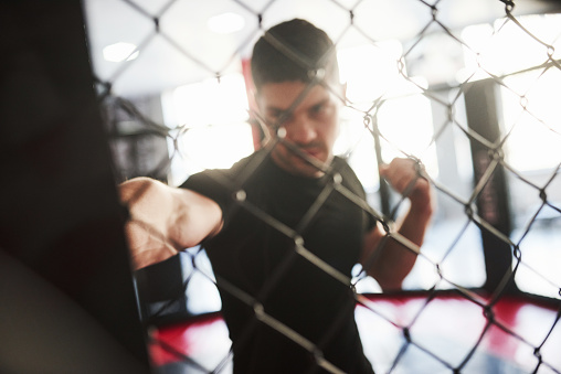 Blurred picture. Strong man is boxing in the gym behind the fence. Haves daily exercise.