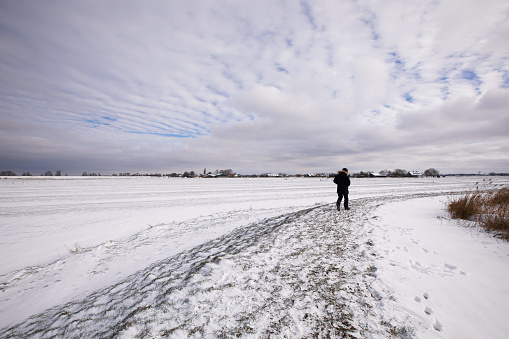 One man is walking on a snowy frozen dike in the winter Dutch countryside