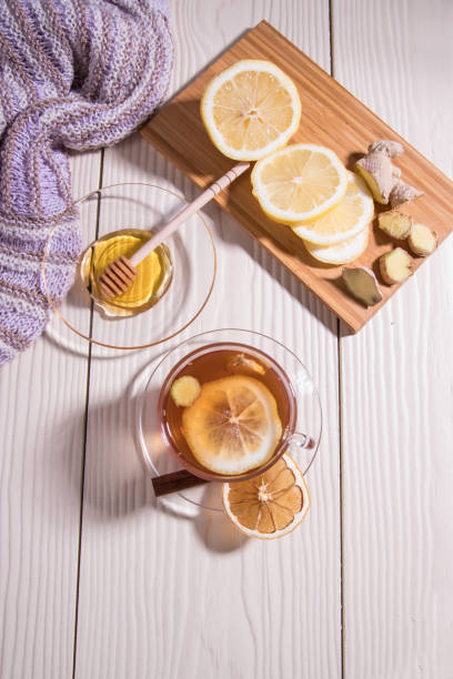 istock Warming vitamin tea with lemon and ginger in a glass Cup, sliced lemon and ginger on a cutting Board, white background. Vertical orientation. 1302413496