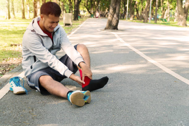 Unhappy young man runner knee injury and pain while sitting on the road in the park. Male athlete suffering from painful knee with accident while running in public park. Injury from workout concept. Unhappy young man runner knee injury and pain while sitting on the road in the park. Male athlete suffering from painful knee with accident while running in public park. Injury from workout concept. sprain stock pictures, royalty-free photos & images