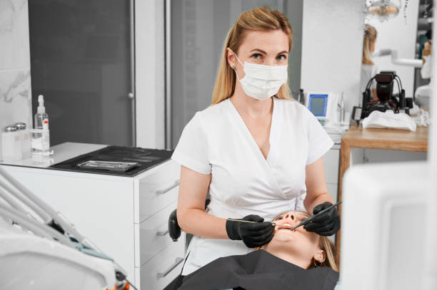 Female dentist at work with patient examining her teeth with dental tools Female dentist at work with patient examining her teeth with dental tools, wearing black latex gloves, face mask and clinic white coat, looking at camera. Copy space. Concept of dentistry. ambulant patient stock pictures, royalty-free photos & images