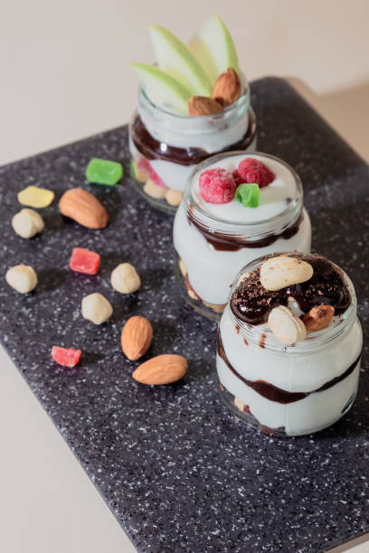 Sweet tasty milk curd creamy food in a glass jar of homemade breakfast. Cheesecake, English Trifle, Eton dessert, tiramisu, zuppa Inglese with nuts, almonds, cashews, hazelnuts, candied fruits and chocolate sauce dulce y sabroso alimento cremoso de cuajada de leche en un tarro de cristal de desayuno casero. tarta de queso, trifle inglés, postre eton, tiramisú, zuppa inglese con nueces, almendras, anacardos, avellanas, frutas confitadas y salsa de chocolate