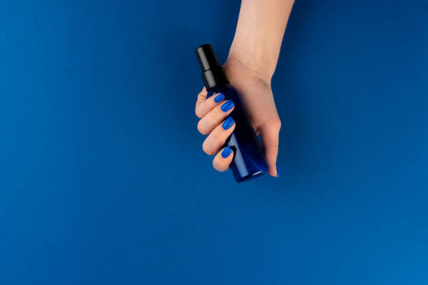 istock Female hands holding cosmetics container in hands against blue background 1302419860
