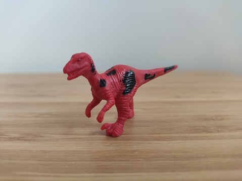 A close-up of a miniature plastic pachycephalosaurus kids toy on a light wooden table. Useful for tabletop board games articles, paleontological kids friendly campaigns and children's educational books.