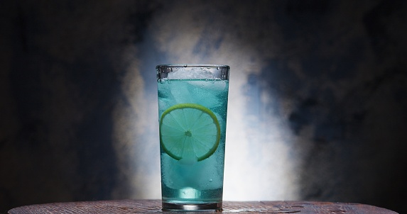 Turquoise colored cold drink  with lime and ice cubes