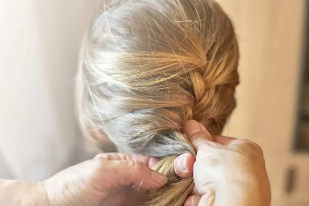 Grandma braids granddaughter's hairs. Queue of hair. Sunlight comes from the left.