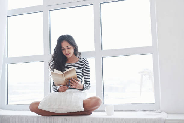 istock Girl reading book while sitting on the windowsill. Having free day 1302423432