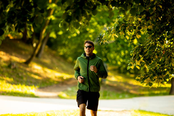 Handsome athletic young man running while doing workout in sunny green park