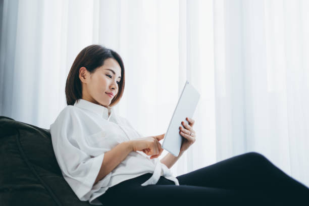 istock Asian woman using her tablet at home by the window 1302428833