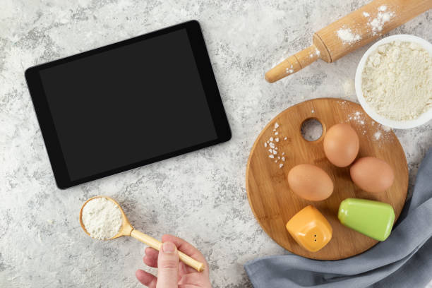 istock Ingredients and tools for baking and tablet with blank screen and place for text or image on white table. recipe, cookbook, cooking courses online template 1302429091