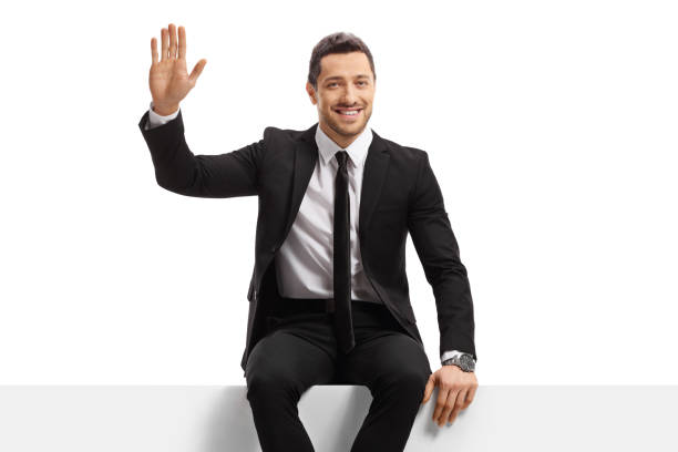 istock Smiling businessman sitting on a panel and waving at the camera 1302430465