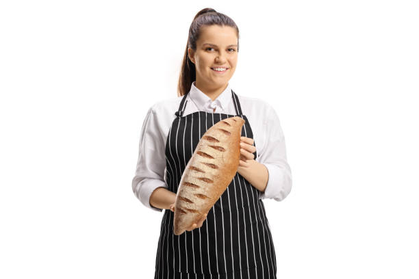 młoda kobieta piekarz sobie fartuch i trzymając bochenek brązowego chleba - chef baker bakery flour zdjęcia i obrazy z banku zdjęć