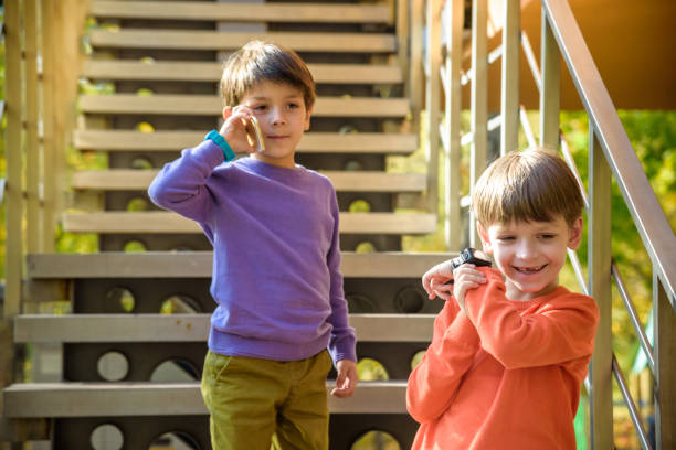 istock Two friends calling each other while standing on stairs outdoor. One boy has mobile phone, other has smart watch with GPS. Protection and safe communication with children concept 1302432432
