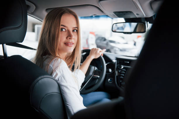 喜びに満ちた気分。現代の黒いインテリアで新しい車に座って美しいブロンドの女の子 - owner women car rear view mirror ストックフォトと画像