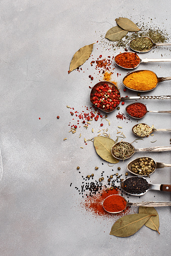 Various colorful spices and herbs in vintage silver spoons on gray concrete background. Overhead view, copy space. Food background