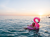 Woman watches sunrise while swimming with inflatable flamingo