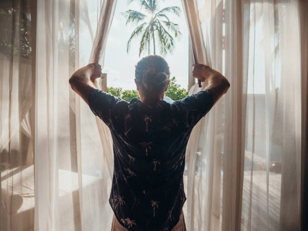 istock Man opening curtains in hotel room at sunrise 1302447094