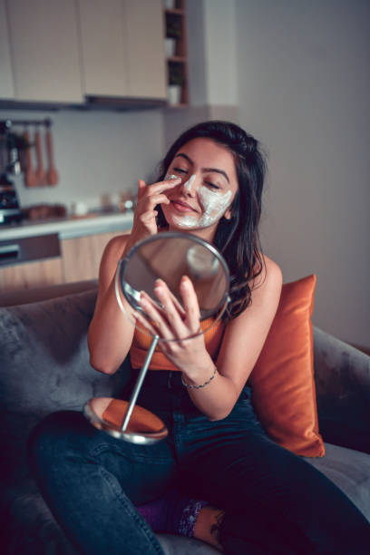 istock Cute Female Applying Face Mask In Mirror 1302447150