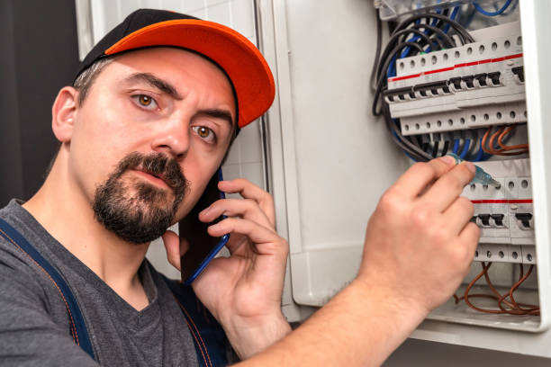 istock Electrician checking fuse box, looking at camera and using smart phone 1302447237