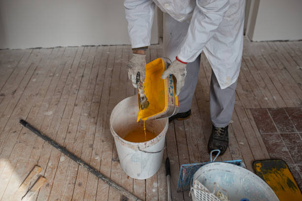 Manual worker pouring yellow paint into bigger plastic bucket