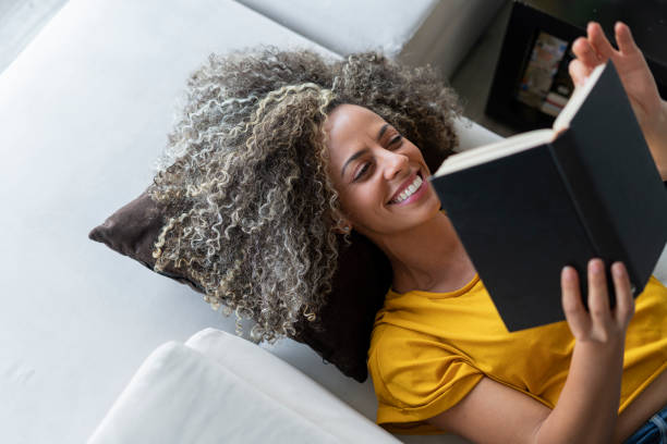 istock Beautiful woman lying on her sofa smiling while reading her book 1302452011