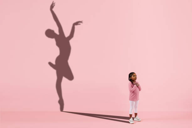 Childhood and dream about big and famous future. Conceptual image with girl and shadow of fit female ballet dancer on coral pink background Childhood and dream about big and famous future. Conceptual image with girl and drawned shadow of female ballet dancer on coral pink background. Childhood, dreams, imagination, education concept. ballerina shadow stock pictures, royalty-free photos & images