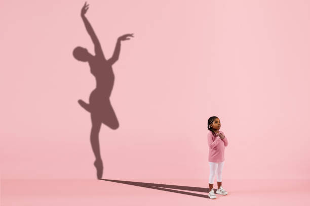 Childhood and dream about big and famous future. Conceptual image with girl and shadow of fit female ballet dancer on coral pink background Childhood and dream about big and famous future. Conceptual image with girl and drawned shadow of female ballet dancer on coral pink background. Childhood, dreams, imagination, education concept. forward athlete stock pictures, royalty-free photos & images