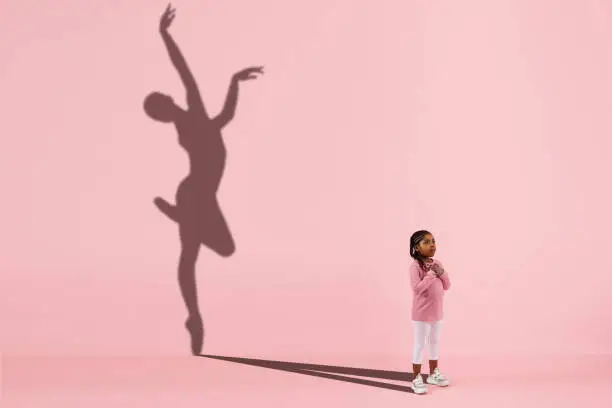 Photo of Childhood and dream about big and famous future. Conceptual image with girl and shadow of fit female ballet dancer on coral pink background