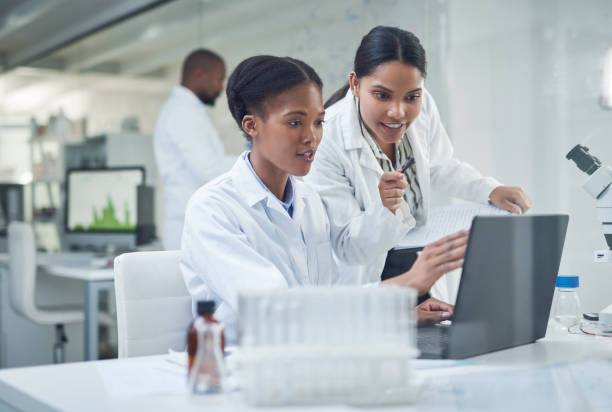 Improving lives one collaboration at a time Shot of two young scientists using a laptop in a laboratory scientist stock pictures, royalty-free photos & images