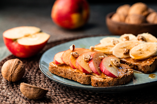 Toasts with peanut butter, apple, banana, walnut and honey. Healthy vegetarian breakfast concept.