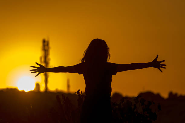 Shot of an unrecognizable child cheering in happiness against sunset. Horizontal shot.