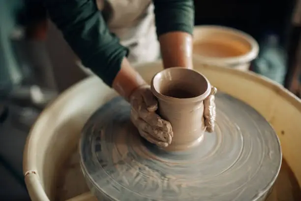 Photo of Child hands make earthenware cup on pottery wheel.
