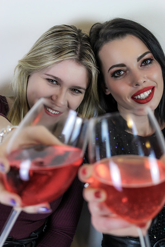 Two girls toast to celebrate an event, and advance their glasses towards the camera