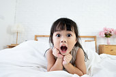 An asian toddler girl 3 years old waking up in bed with surprising expression.