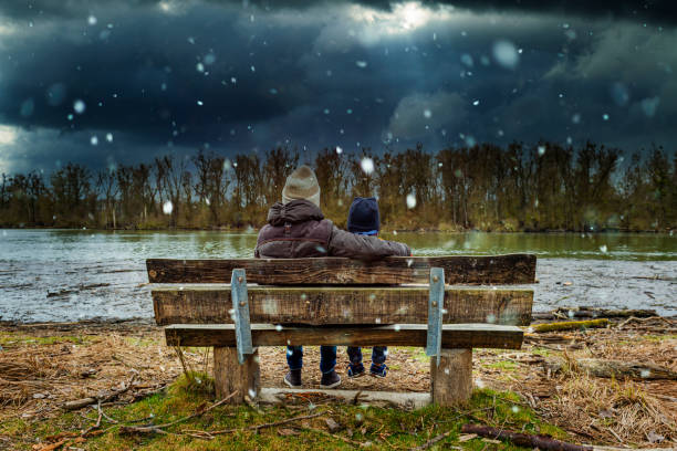 istock mother and child resting on a bench. It is just beginning to snow 1302466488